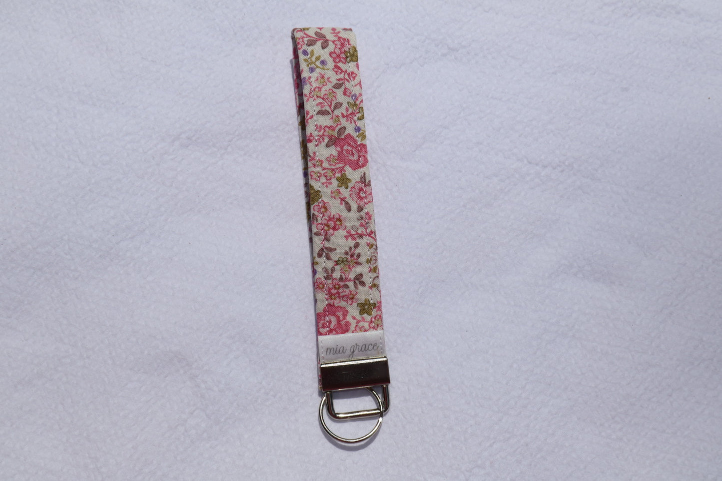 Fabric key fob with a pink and purple floral patten with butterflies and a Mia grace brand label and a key ring