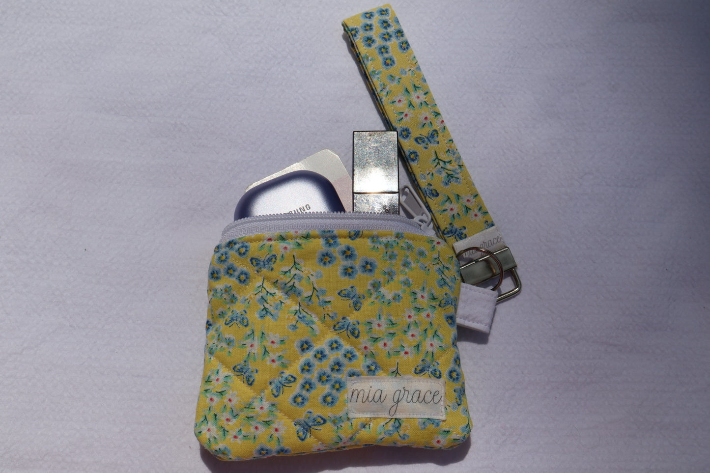 yellow and blue floral with butterflies wallet sized pouch with a 'mia grace' brand label, zipper closure, and a hoop for a key ring to be attached with a matching keychain wristlet that is sold separately.