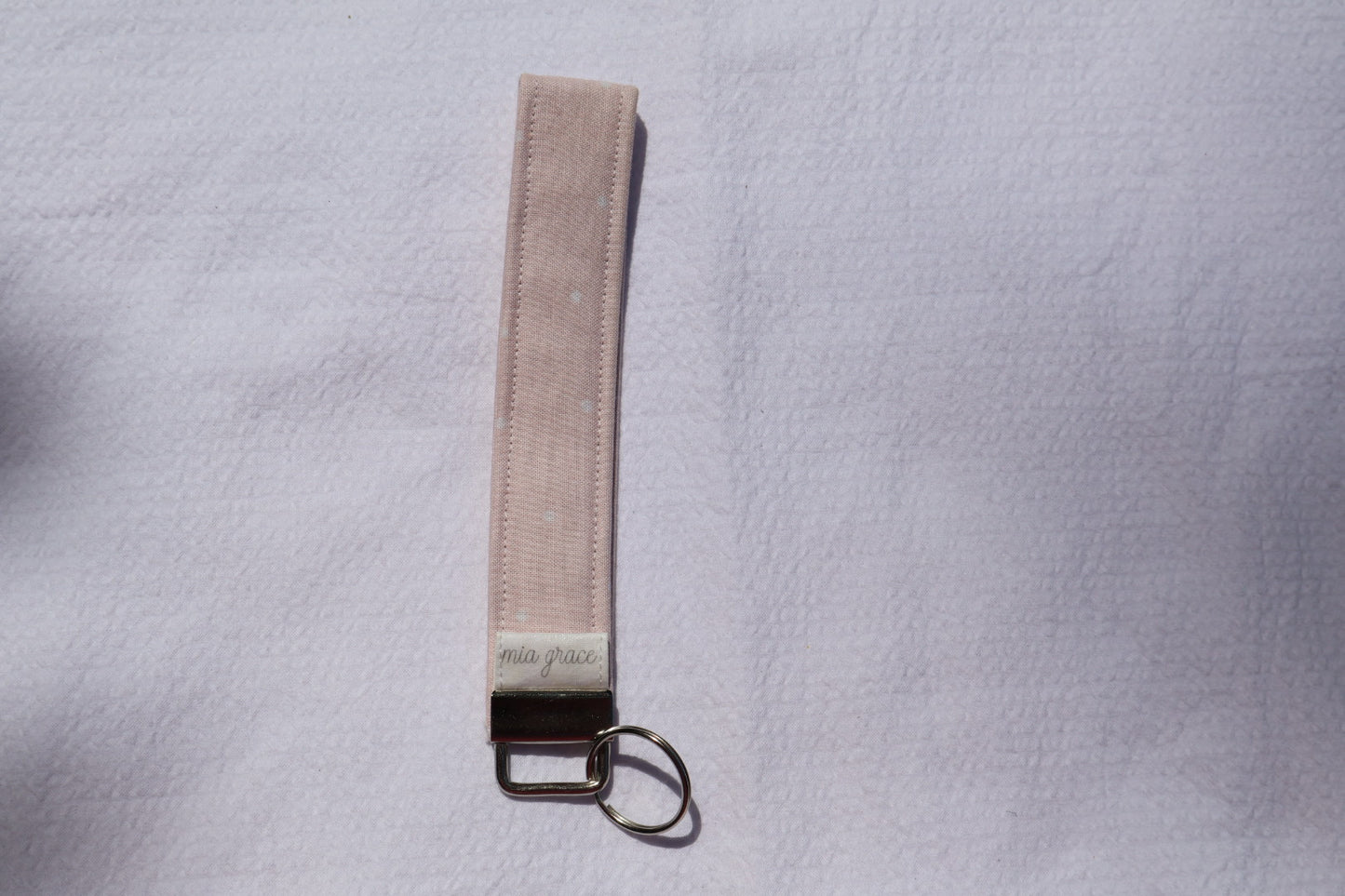 Fabric key fob with a pink fabric and white polka dots pattern and a Mia grace brand label and a key ring