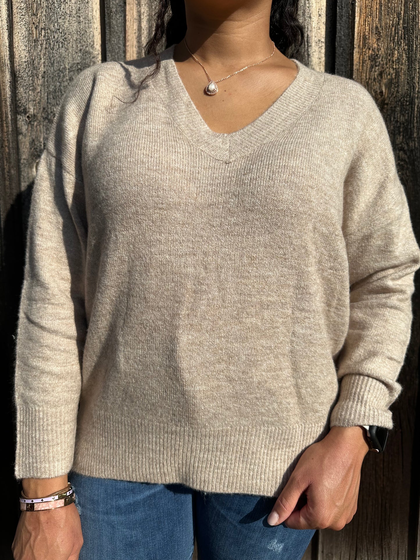 A woman wearing a light taupe v-neck knit sweater with drop shoulders and ribbed trim.