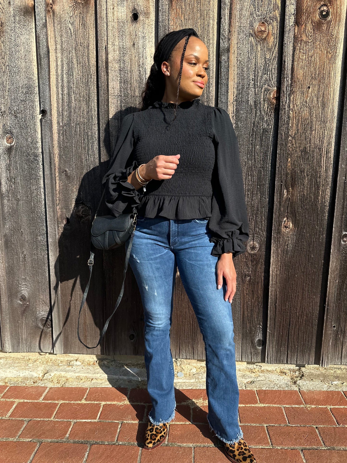 A person wearing a black smocked peplum top with long sleeves and a ruffled neckline.