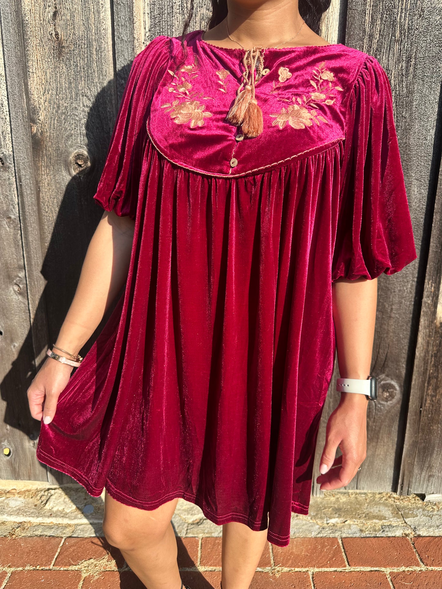 Maroon Dress with pleated detailing and scallop stitching details with floral embroidery on yoke and functional buttons with a tie tassel. Back paneling also has the floral embroidery detailing. The dress is short sleeve with flowy balloon sleeves.