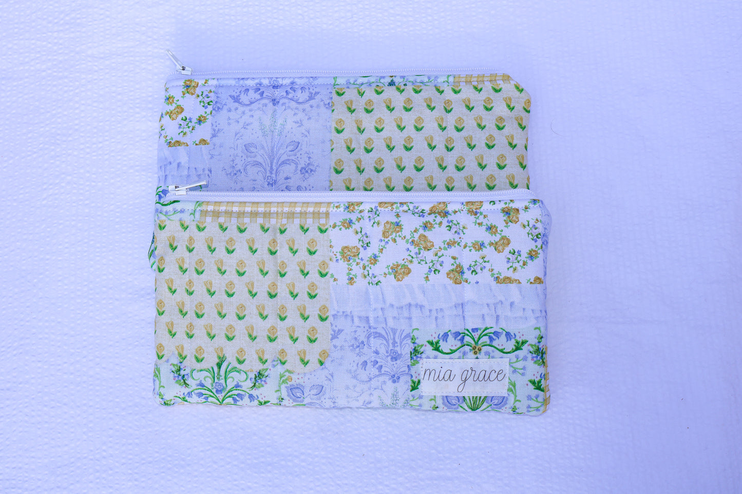 Patchwork blue, yellow, and green fabric quilted pouch with a Mia grace branding label