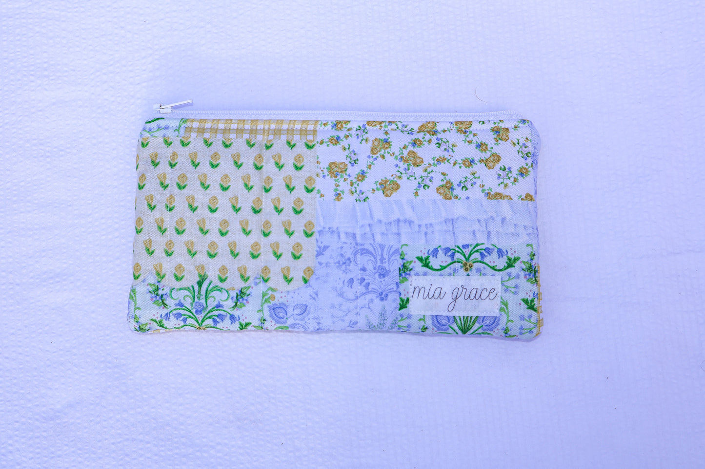 Patchwork blue, yellow, and green fabric quilted pouch with a Mia grace branding label