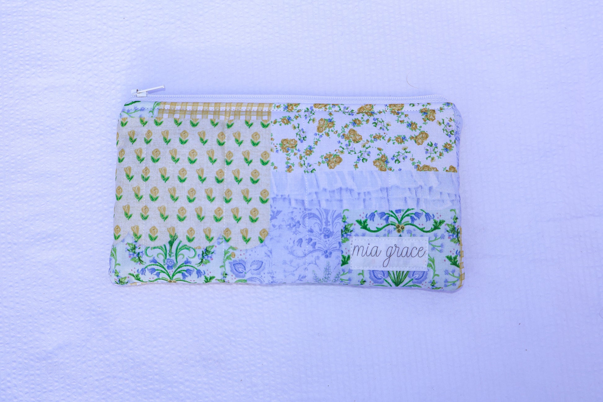 Patchwork blue, yellow, and green fabric quilted pouch with a Mia grace branding label