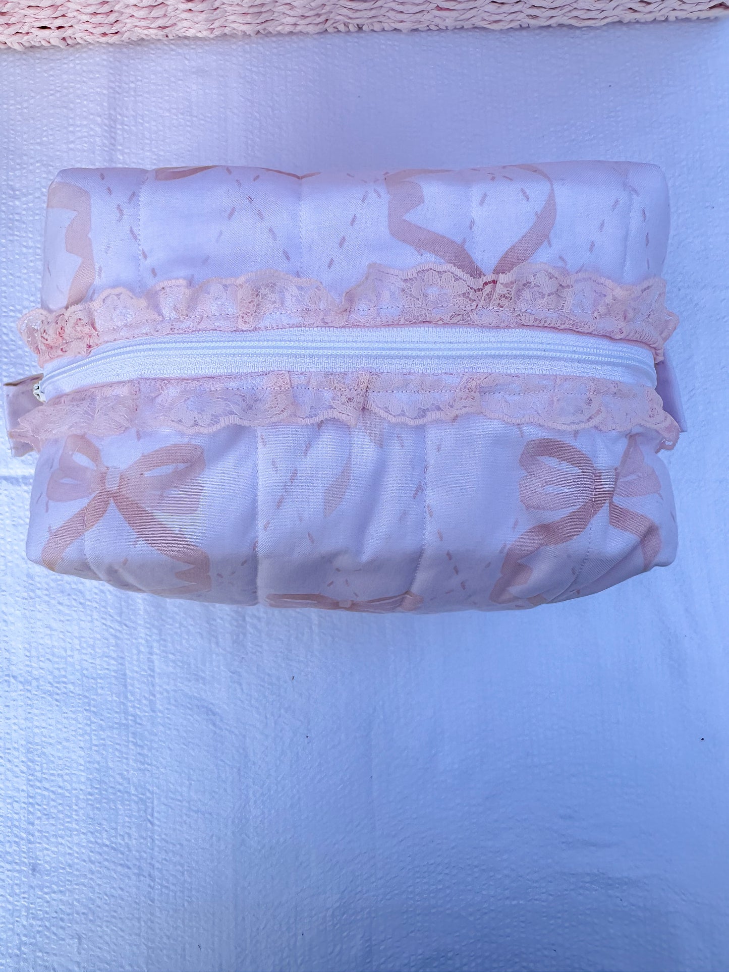 soft pink with pink bows quilted boxy pouch with a Mia Grace brand label and a white zipper and pull tabs. zipper has a pink lace trim 