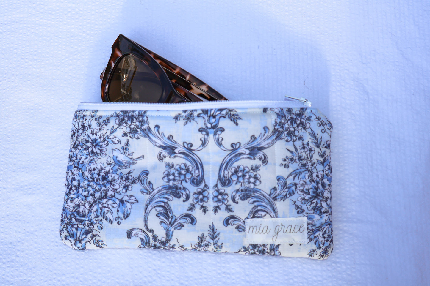 Blue floral patterned pouch with a zipper closure and a Mia grace brand label 