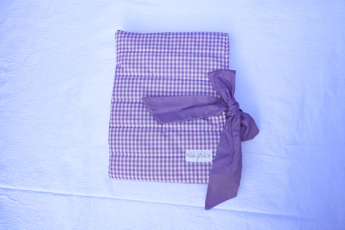 Purple gingham quilted bible or book sleeve with a purple fabric bow tied closure and a Mia grace brand label on the front bottom right. 