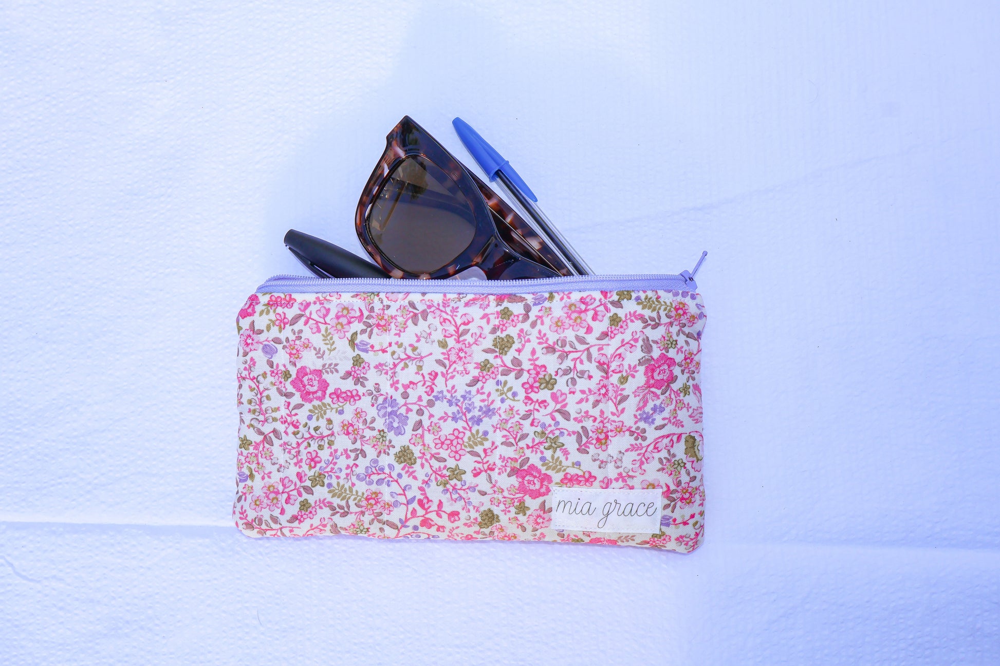 Fabric pouch with pink and purple floral pattern and 'mia grace' branding label 