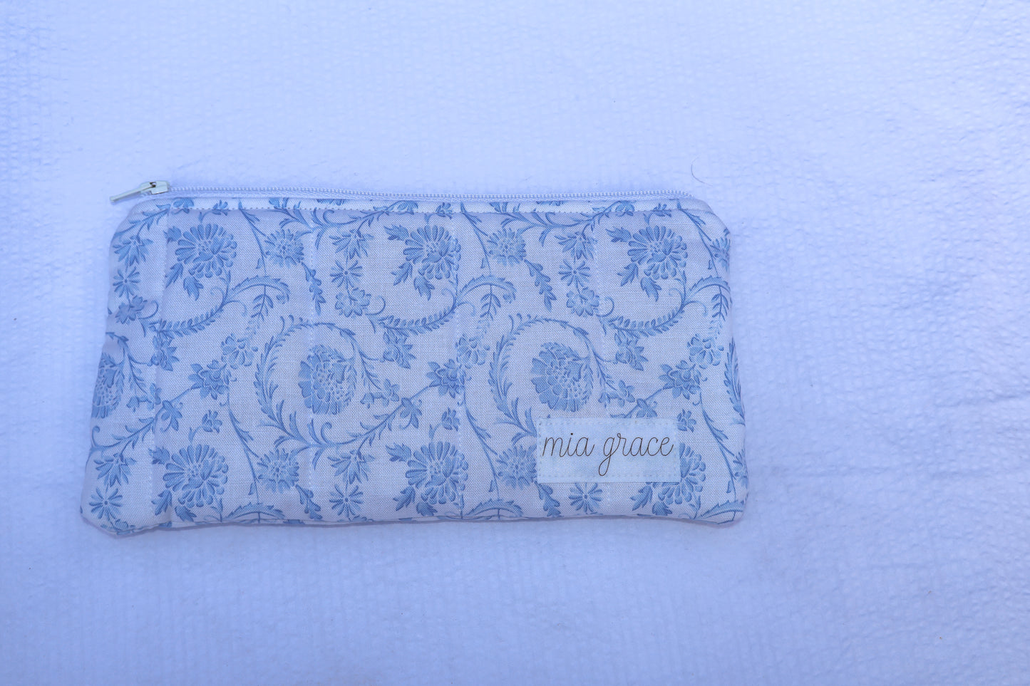 Fabric pouch with blue floral pattern and 'mia grace' branding label 