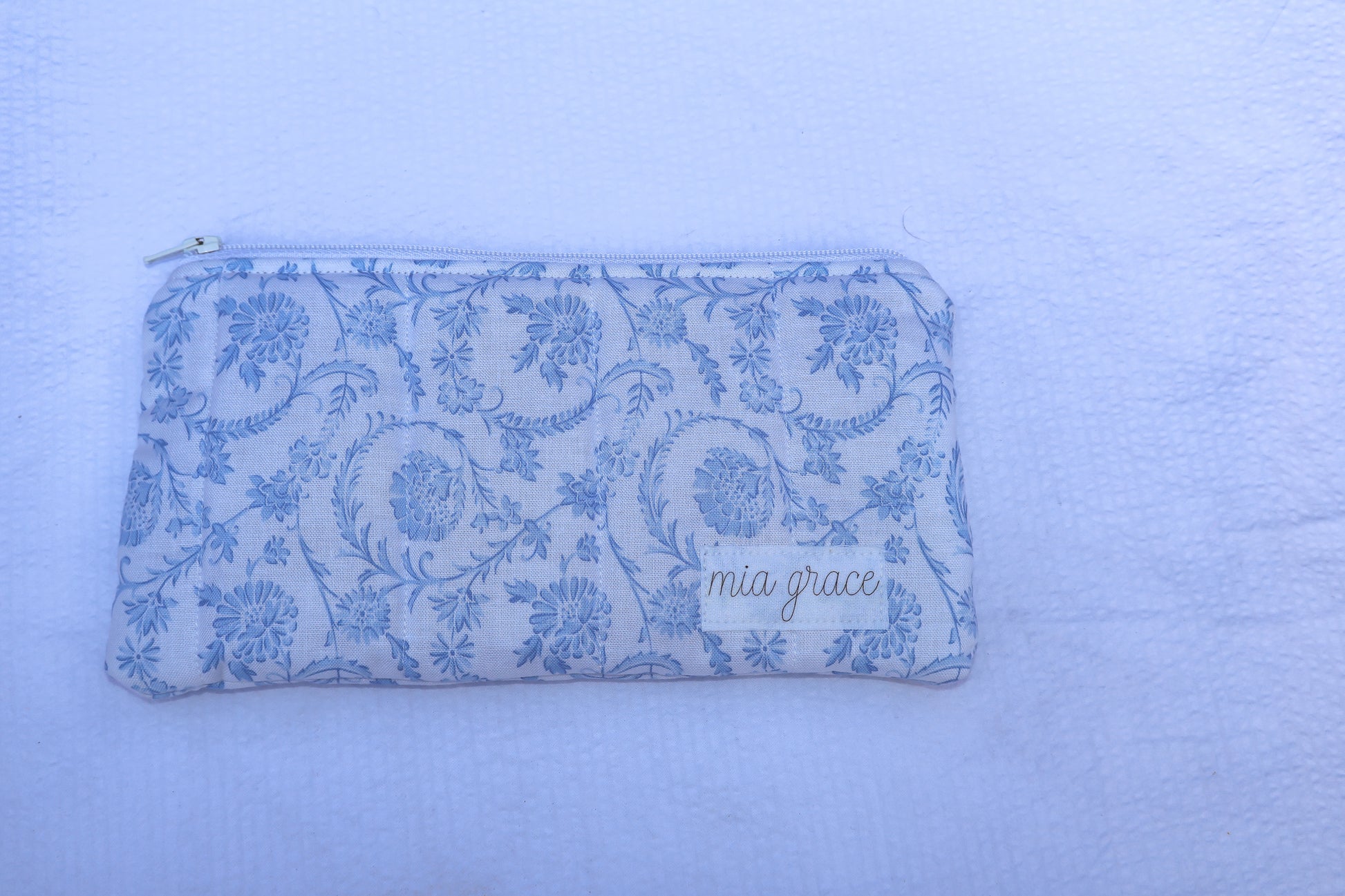 Fabric pouch with blue floral pattern and 'mia grace' branding label 