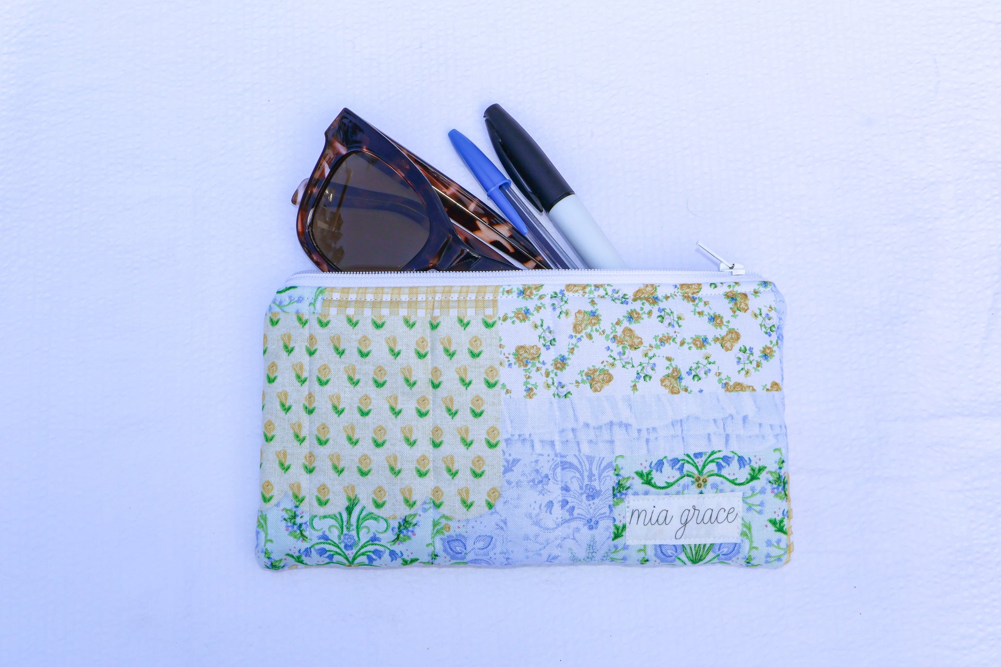 Patchwork blue, yellow, and green fabric quilted pouch with a Mia grace branding label