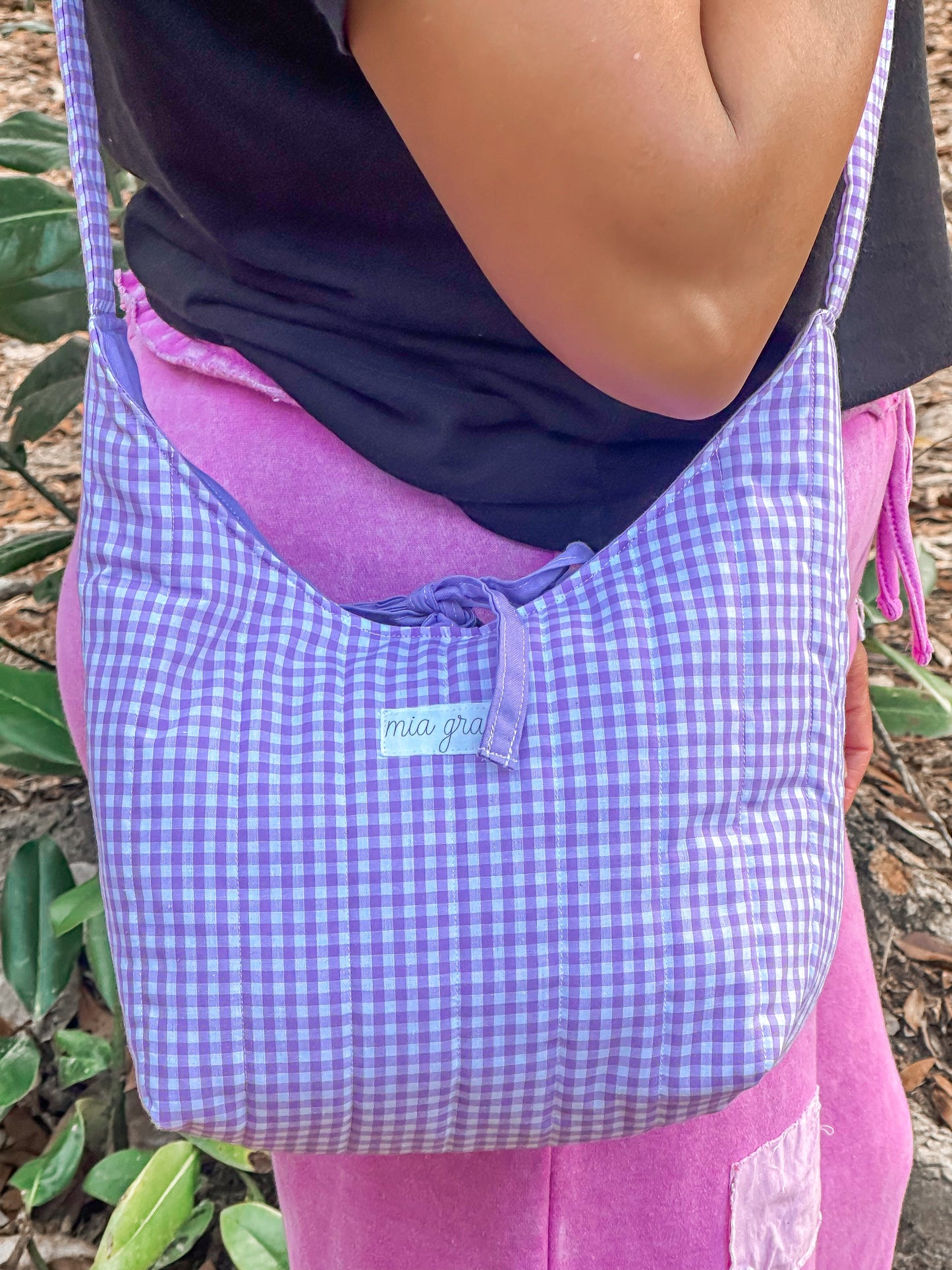 close up of a woman wearing a purple gingham shoulder bag with a Mia Grace brand label and a purple tie closure to match the purple inner fabric. 