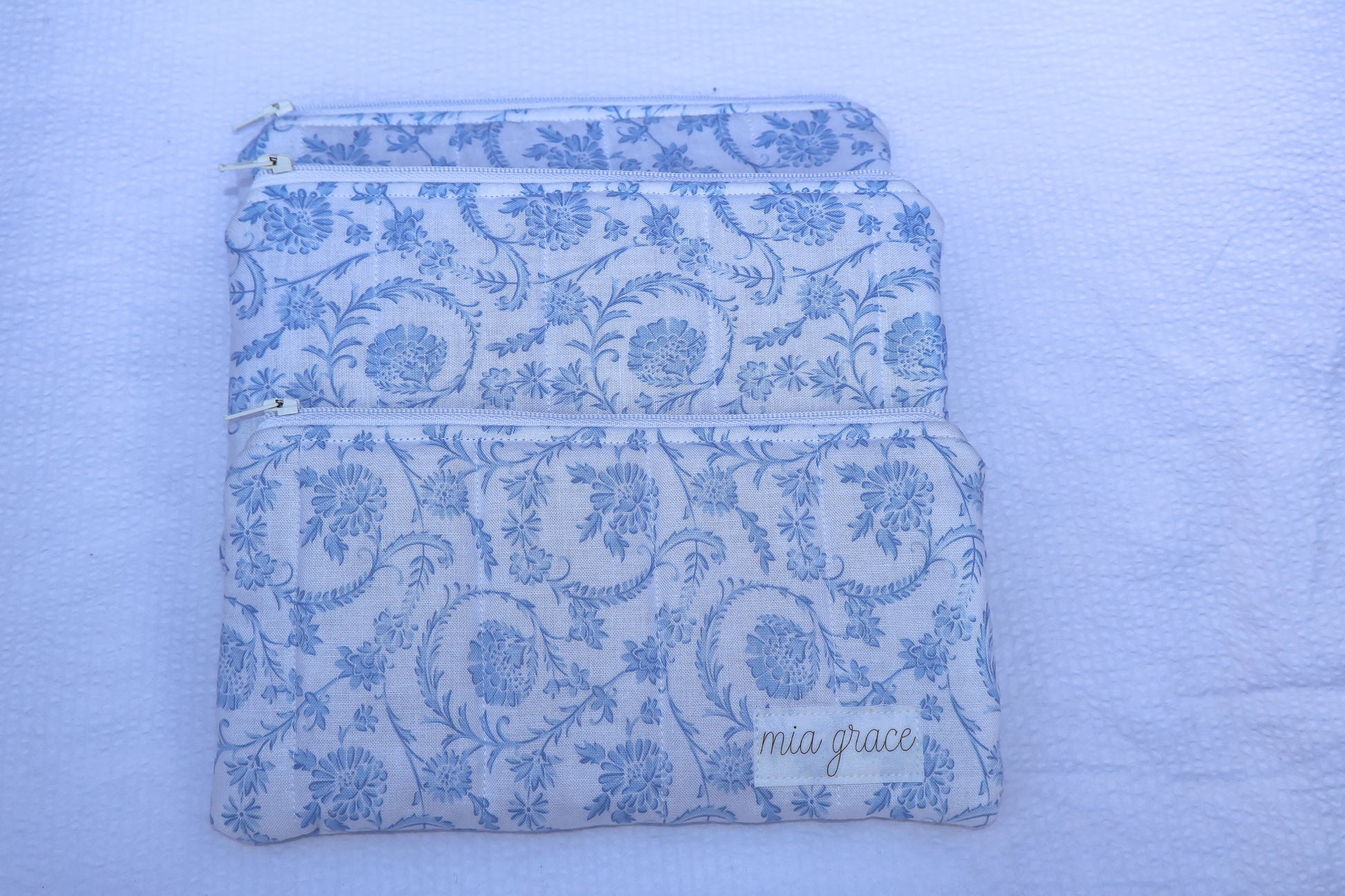 Fabric pouch with blue floral pattern and 'mia grace' branding label 