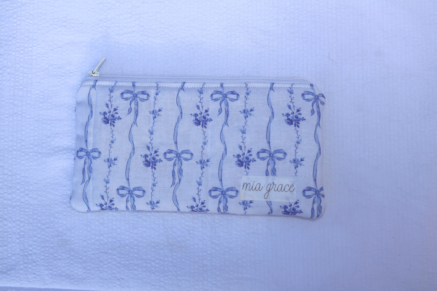 Fabric pouch with blue bow and floral patterns and 'mia grace' branding label 