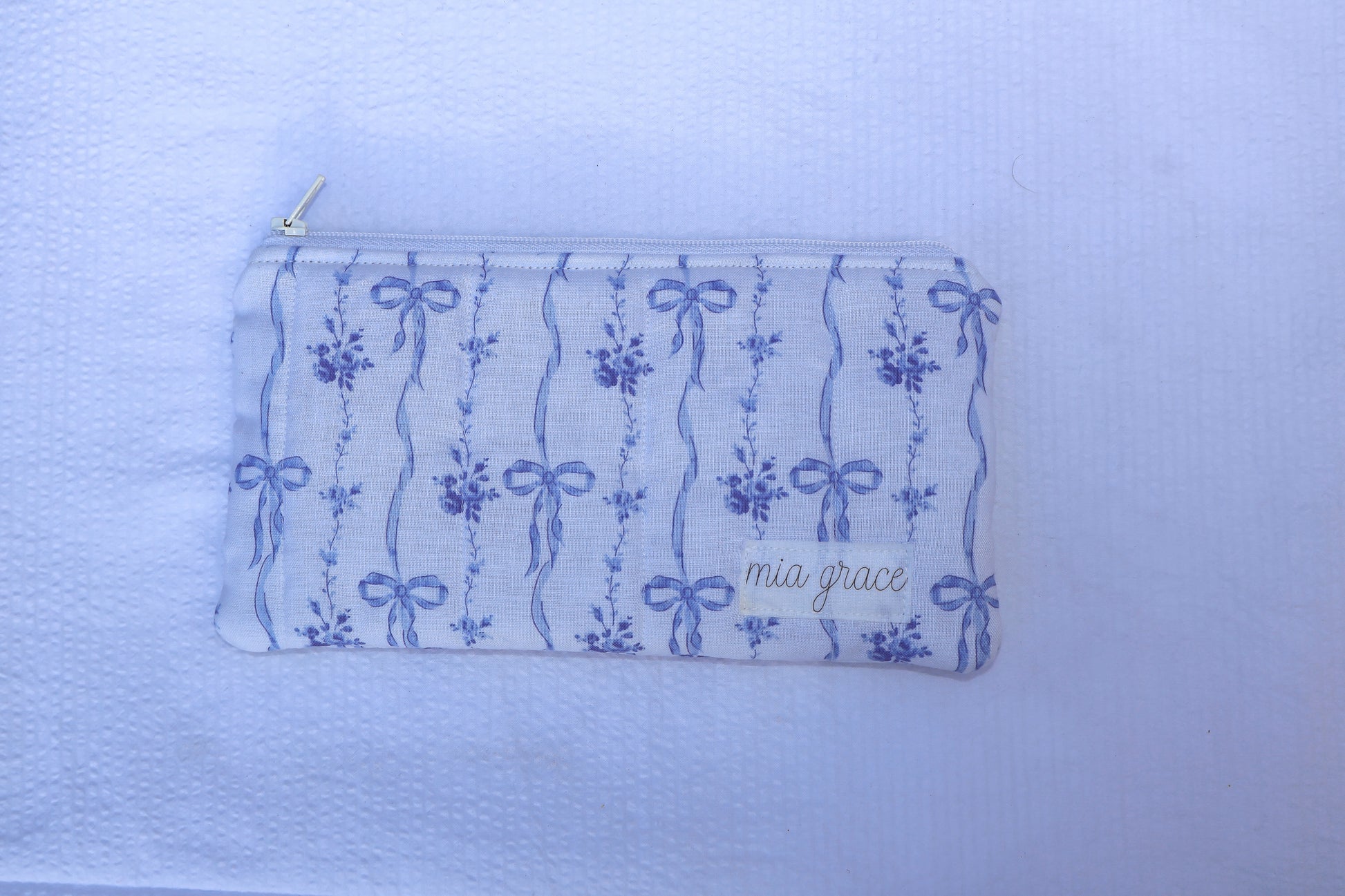 Fabric pouch with blue bow and floral patterns and 'mia grace' branding label 
