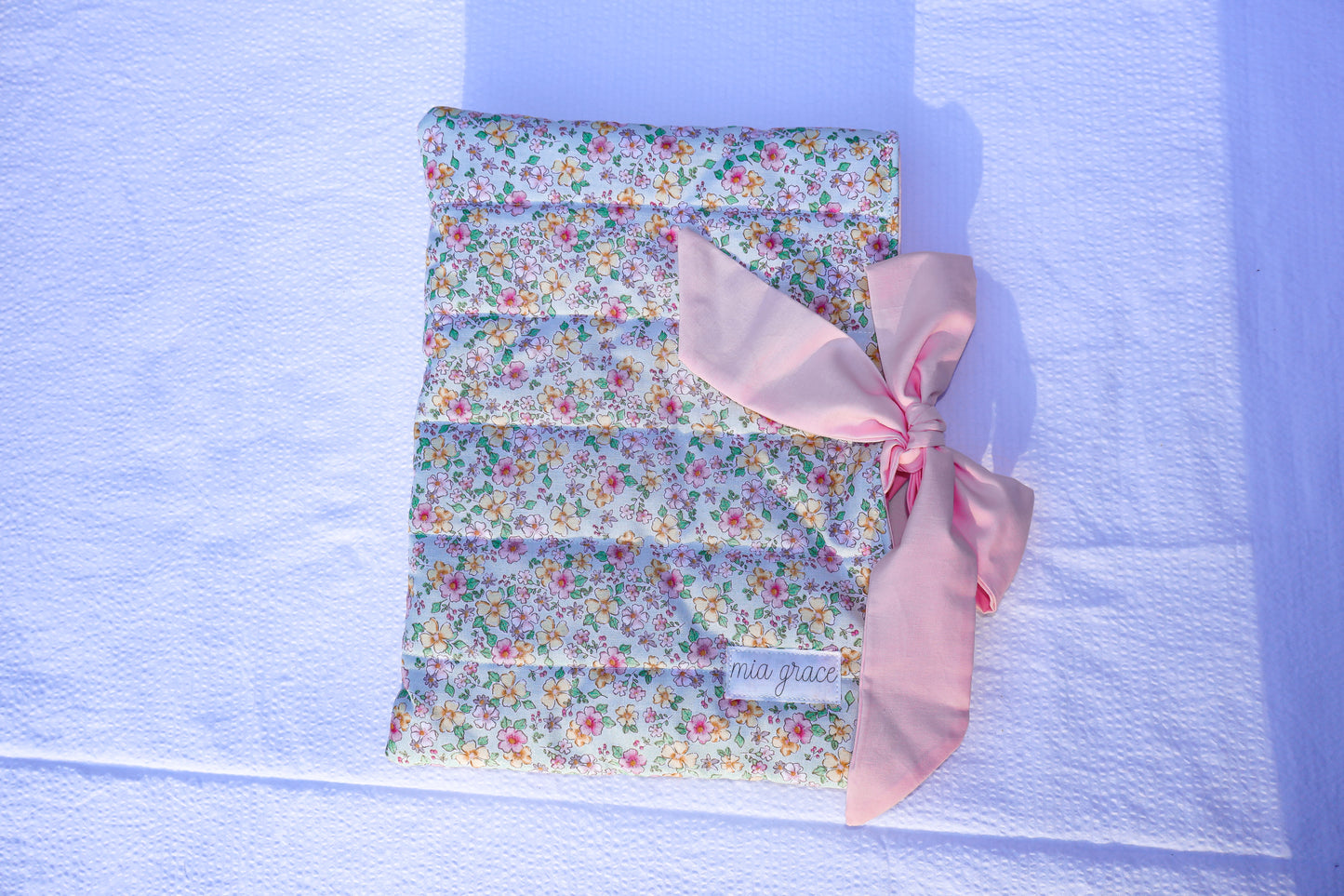 mint green, pink, and yellow floral fabric quilted bible or book sleeve with a soft pink bow tied closure. Mia grace brand label on the front 