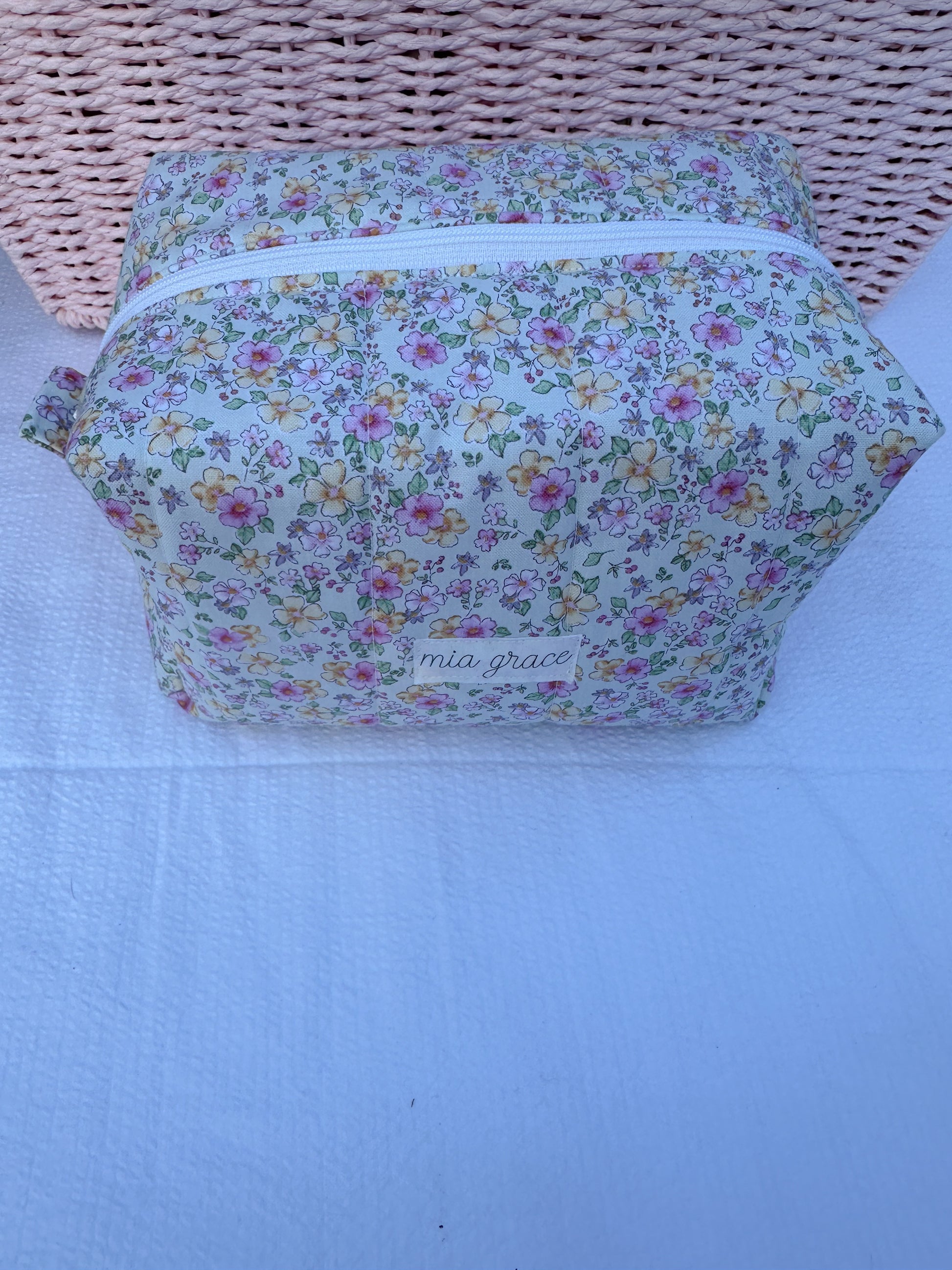 mint color,pink, and yellow  floral-patterned quilted boxy pouch with a Mia Grace brand label and a white zipper and pull tabs.  