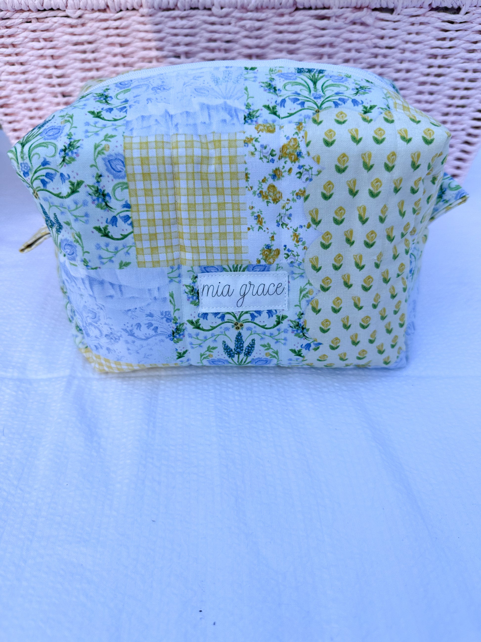 yellow, blue, and green  floral-patchwork quilted boxy pouch with a Mia Grace brand label and a white zipper and pull tabs. 