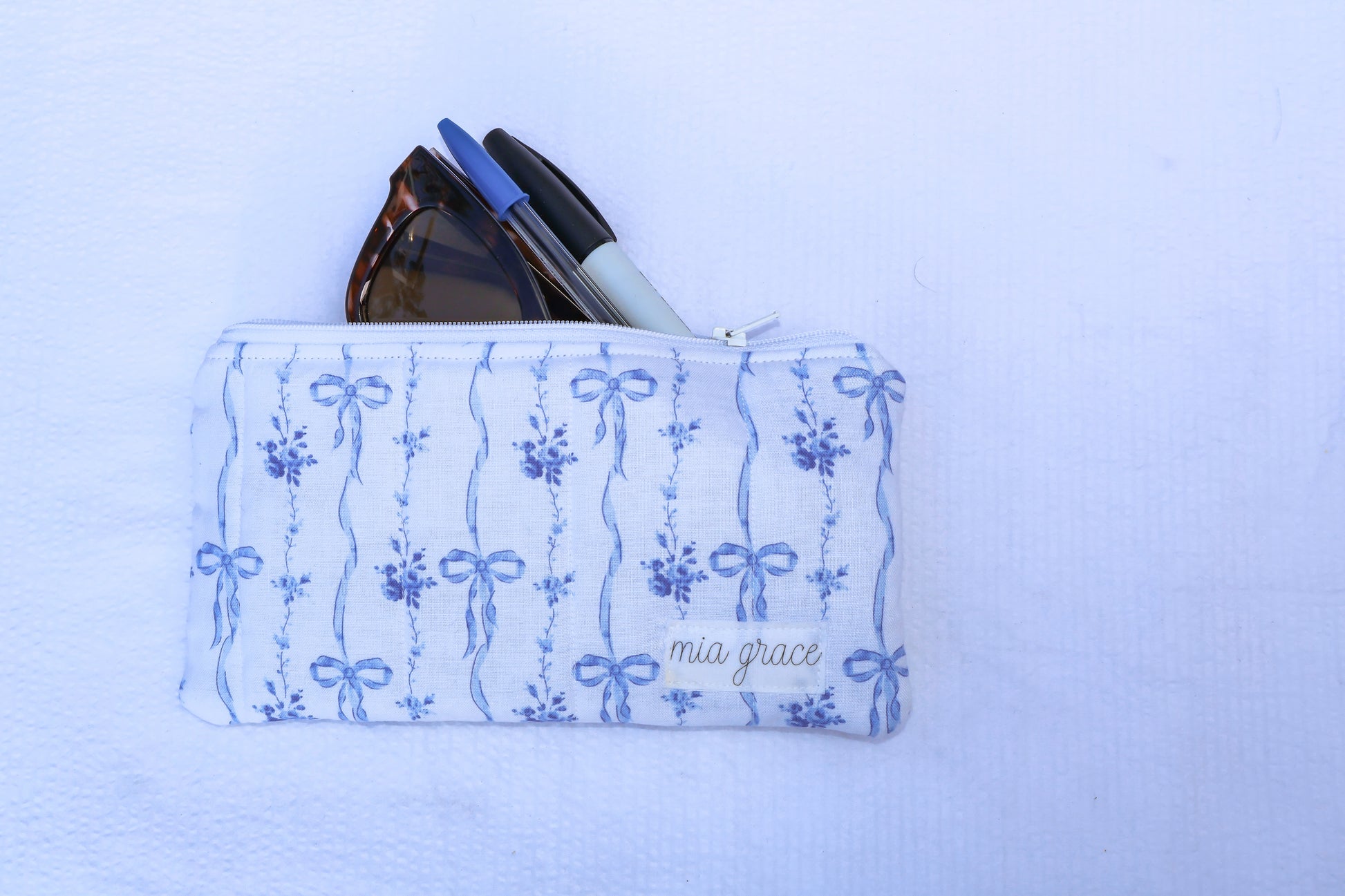 Fabric pouch with blue bow and floral patterns and 'mia grace' branding label 