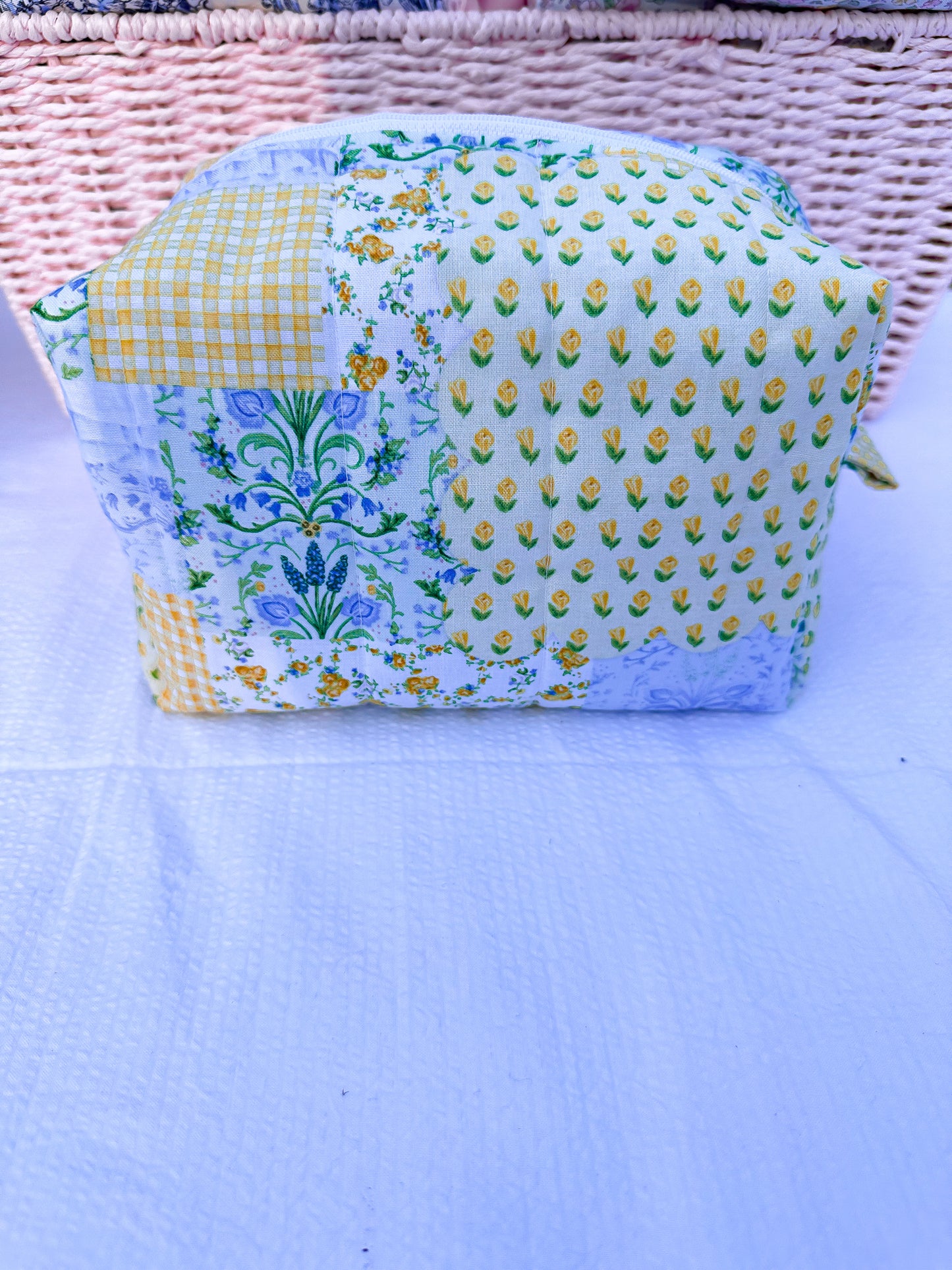 yellow, blue, and green  floral-patchwork quilted boxy pouch with a Mia Grace brand label and a white zipper and pull tabs.