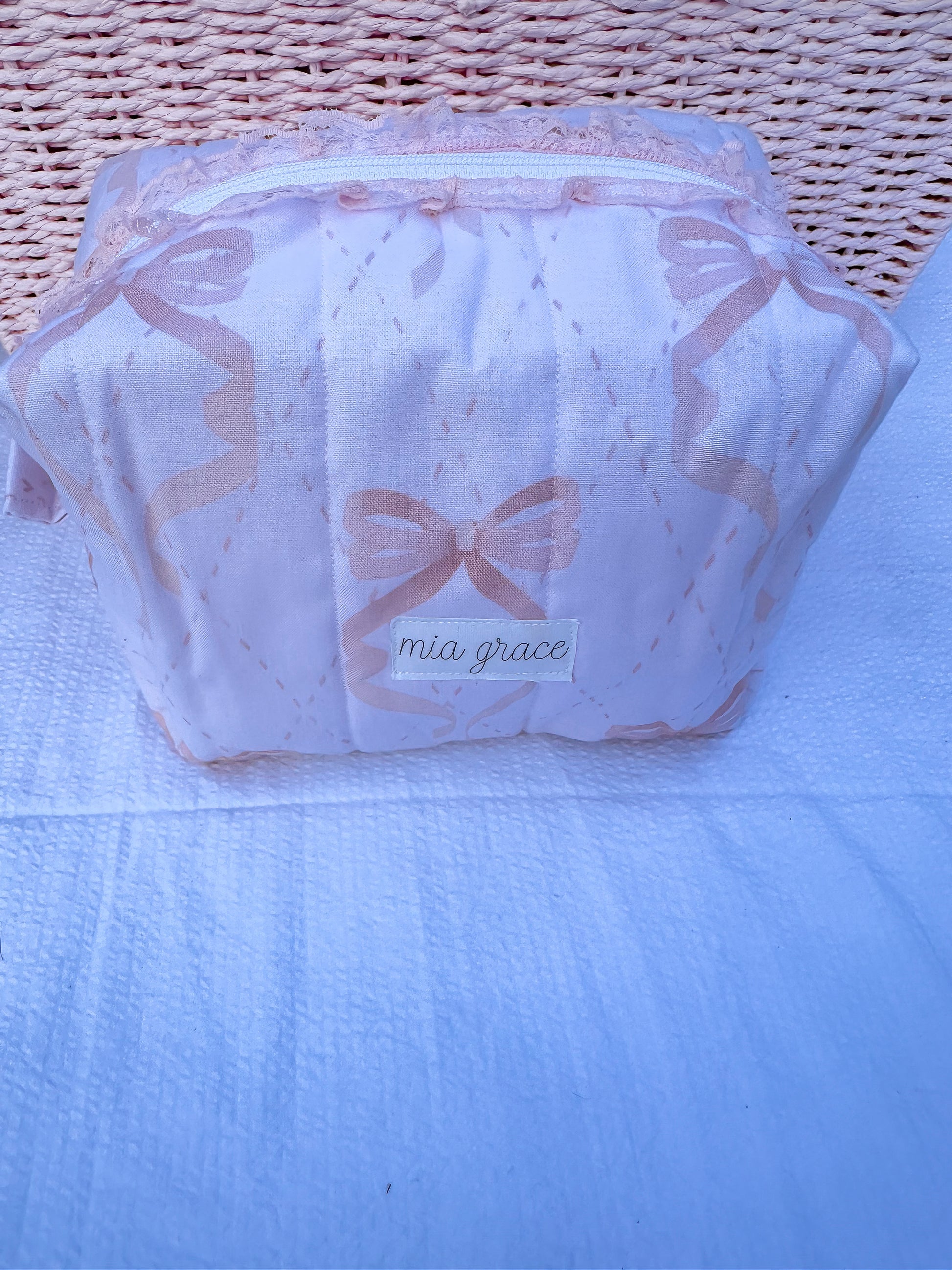 soft pink with pink bows quilted boxy pouch with a Mia Grace brand label and a white zipper and pull tabs. zipper has a pink lace trim 