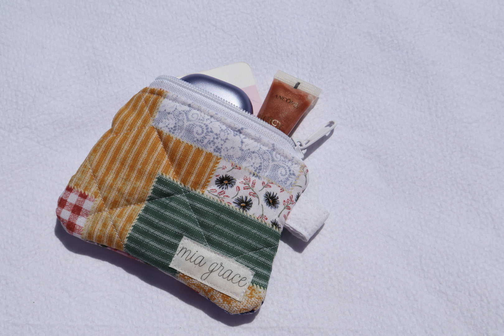 close up of a patchwork fabric wallet sized pouch with a 'mia grace' brand label, zipper closure, and a hoop for a key ring to be attached. 