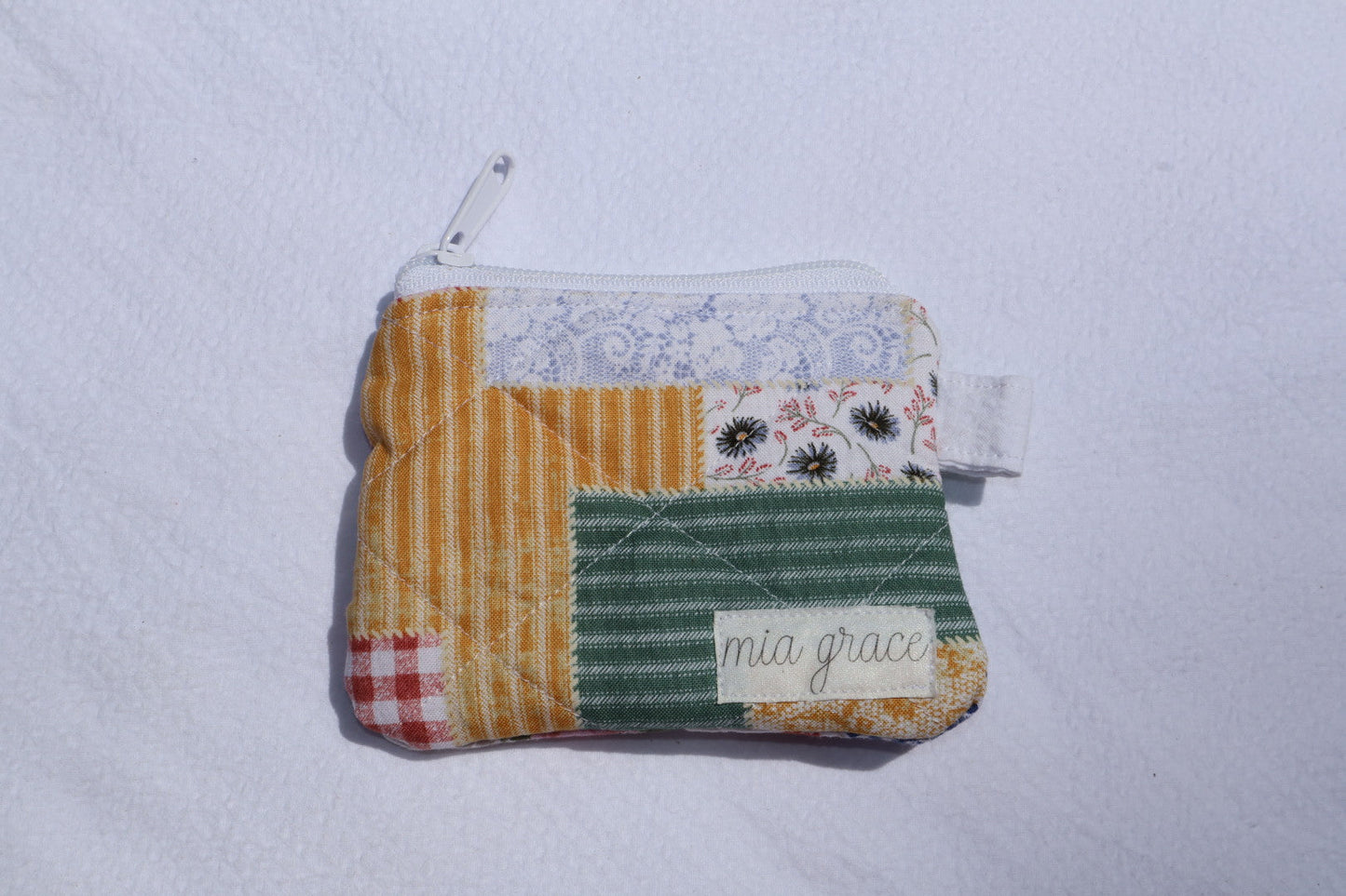 patchwork fabric wallet sized pouch with a 'mia grace' brand label, zipper closure, and a hoop for a key ring to be attached. 