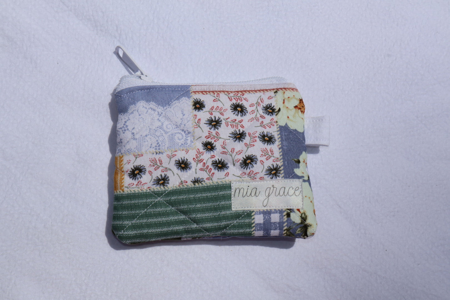 patchwork fabric wallet sized pouch with a 'mia grace' brand label, zipper closure, and a hoop for a key ring to be attached. 