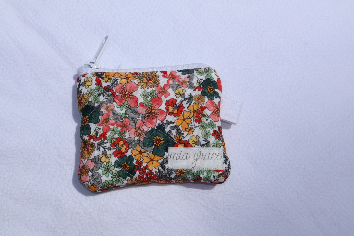yellow, blue, and pink floral wallet sized pouch with a 'mia grace' brand label, zipper closure, and a hoop for a key ring to be attached. 
