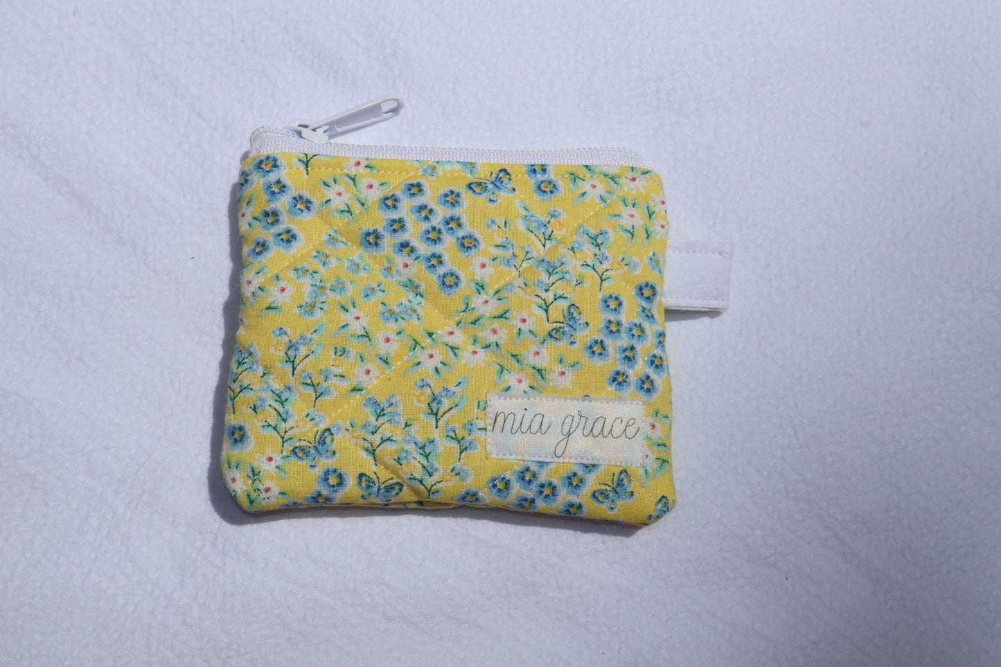 yellow and blue floral with butterflies wallet sized pouch with a 'mia grace' brand label, zipper closure, and a hoop for a key ring to be attached. 