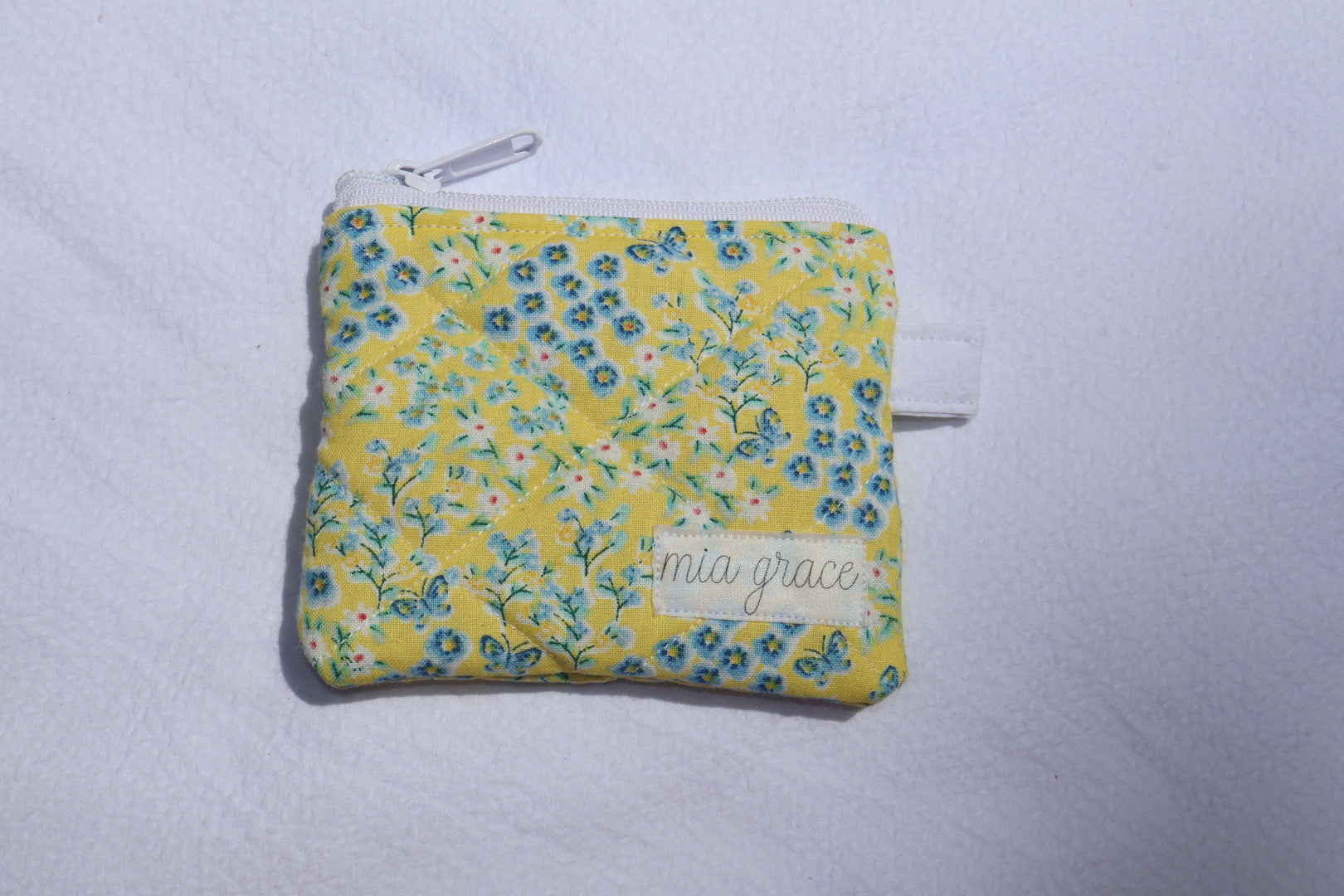 yellow and blue floral with butterflies wallet sized pouch with a 'mia grace' brand label, zipper closure, and a hoop for a key ring to be attached. 