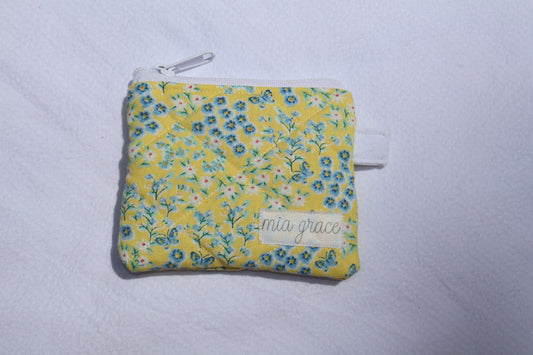 yellow and blue floral with butterflies wallet sized pouch with a 'mia grace' brand label, zipper closure, and a hoop for a key ring to be attached. 
