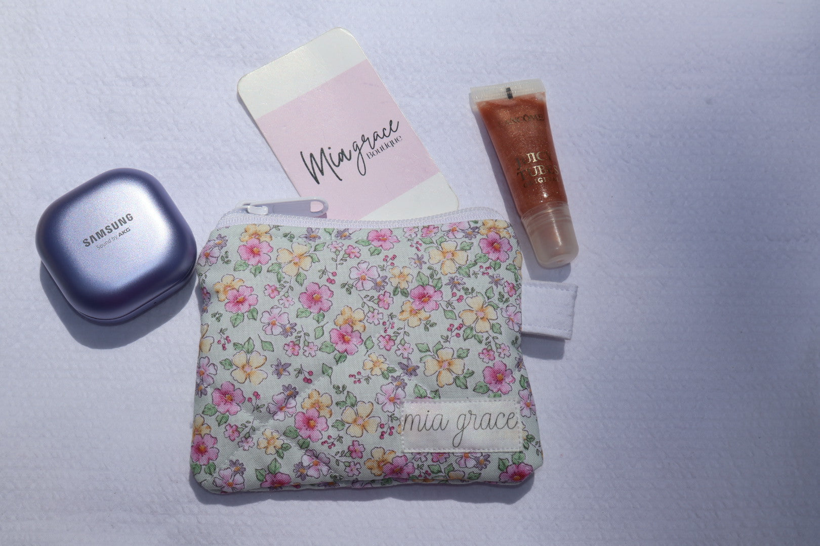 mint, pink, and yellow floral wallet sized pouch with a 'mia grace' brand label, zipper closure, and a hoop for a key ring to be attached. 