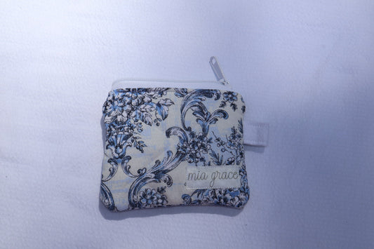 Small  blue and white floral wallet sized pouch with a 'mia grace' brand label, zipper closure, and a hoop for a key ring to be attached. 