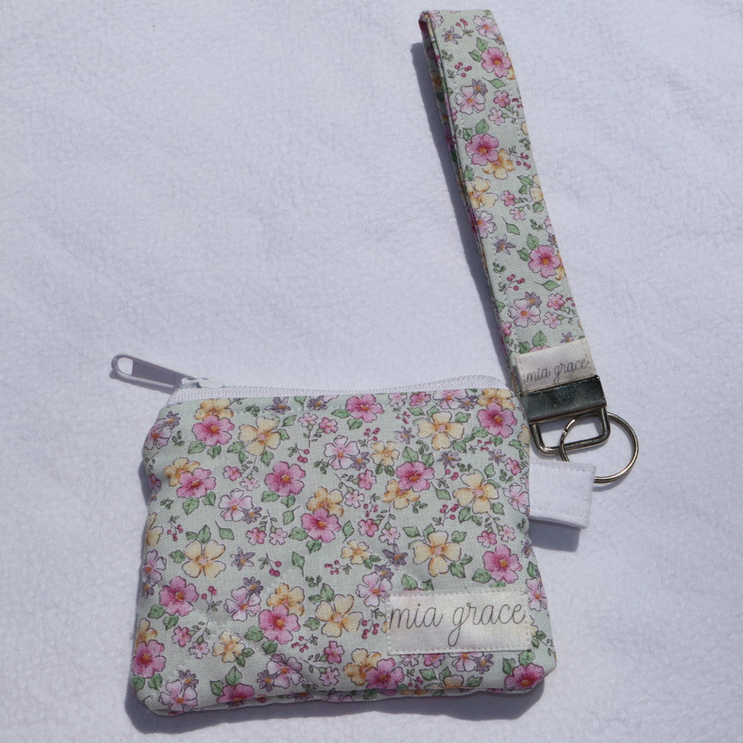 mint, pink, and yellow floral wallet sized pouch with a 'mia grace' brand label, zipper closure, and a hoop for a key ring to be attached with a matching keychain wristlet that is sold separately