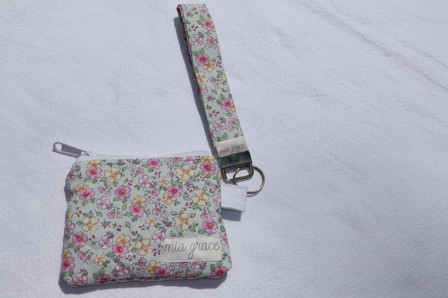 Fabric key fob with a mint, pink, and yellow floral  patten with butterflies and a Mia grace brand label and a key ring with a matching wallet that is sold separately 