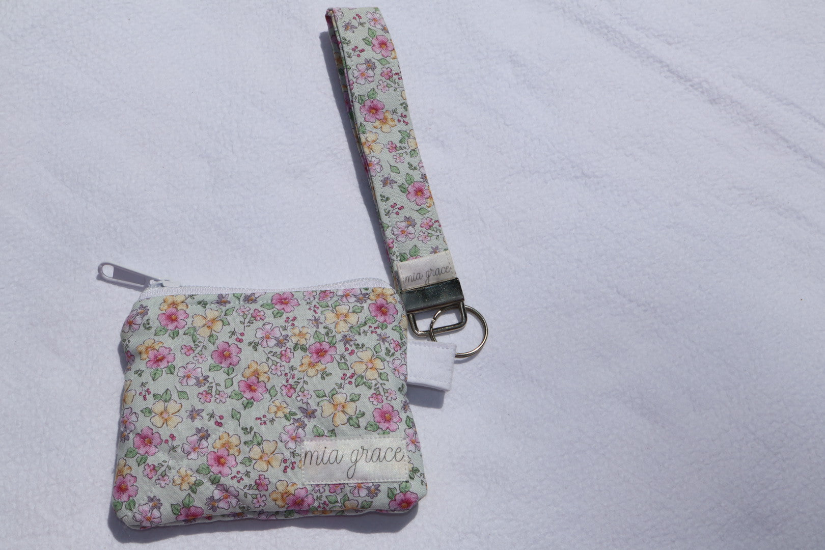 Fabric key fob with a mint, pink, and yellow floral  patten with butterflies and a Mia grace brand label and a key ring with a matching wallet that is sold separately 