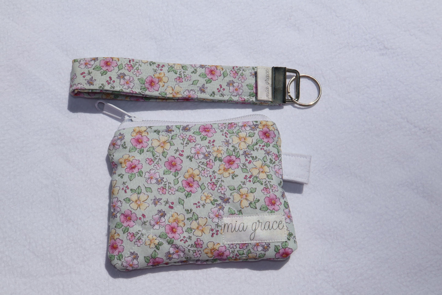 mint, pink, and yellow floral wallet sized pouch with a 'mia grace' brand label, zipper closure, and a hoop for a key ring to be attached with a matching wristlet that is sold separately. 