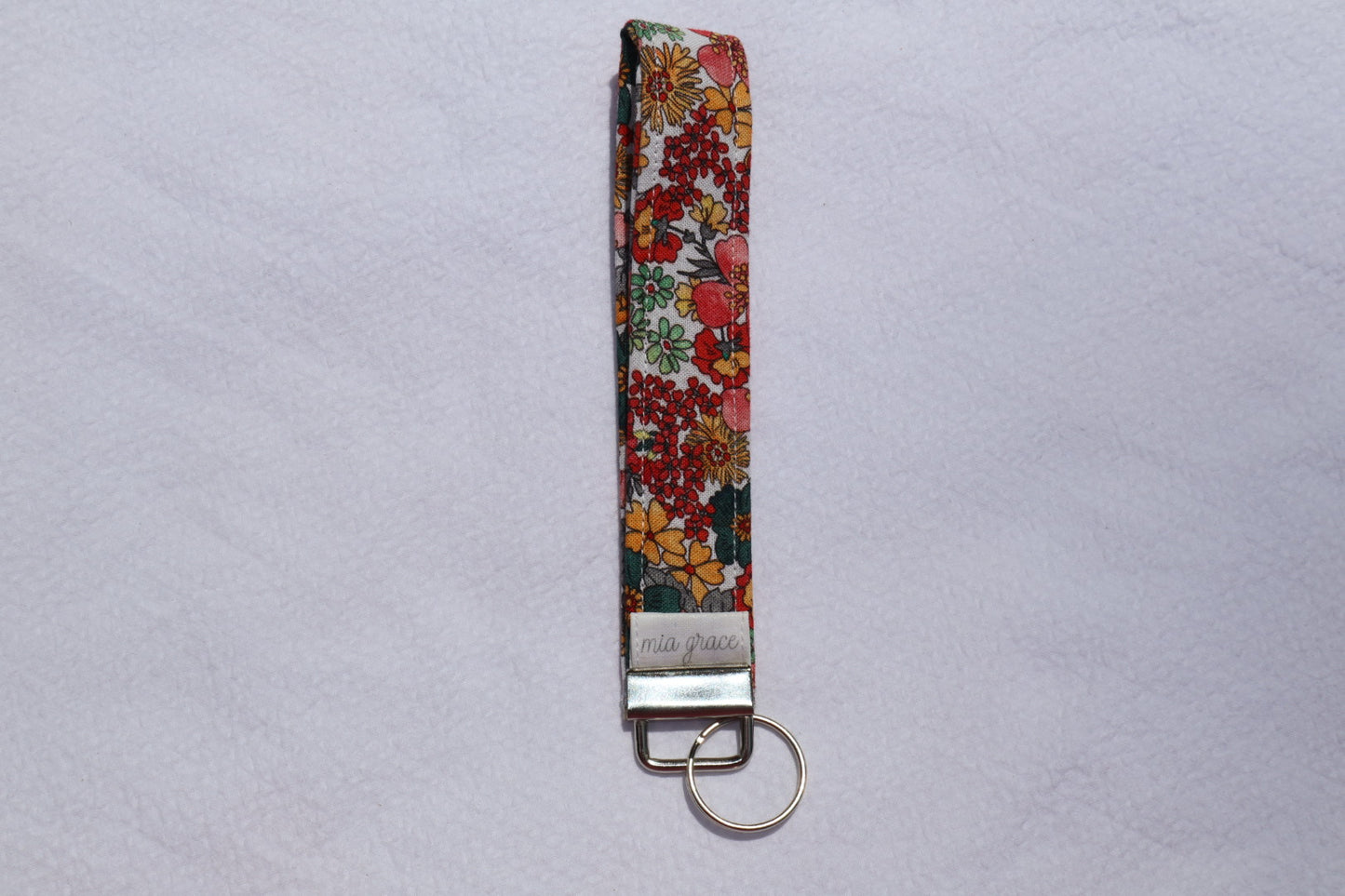 Fabric key fob with a yellow, blue, gray, and pink floral  patten with butterflies and a Mia grace brand label and a key ring