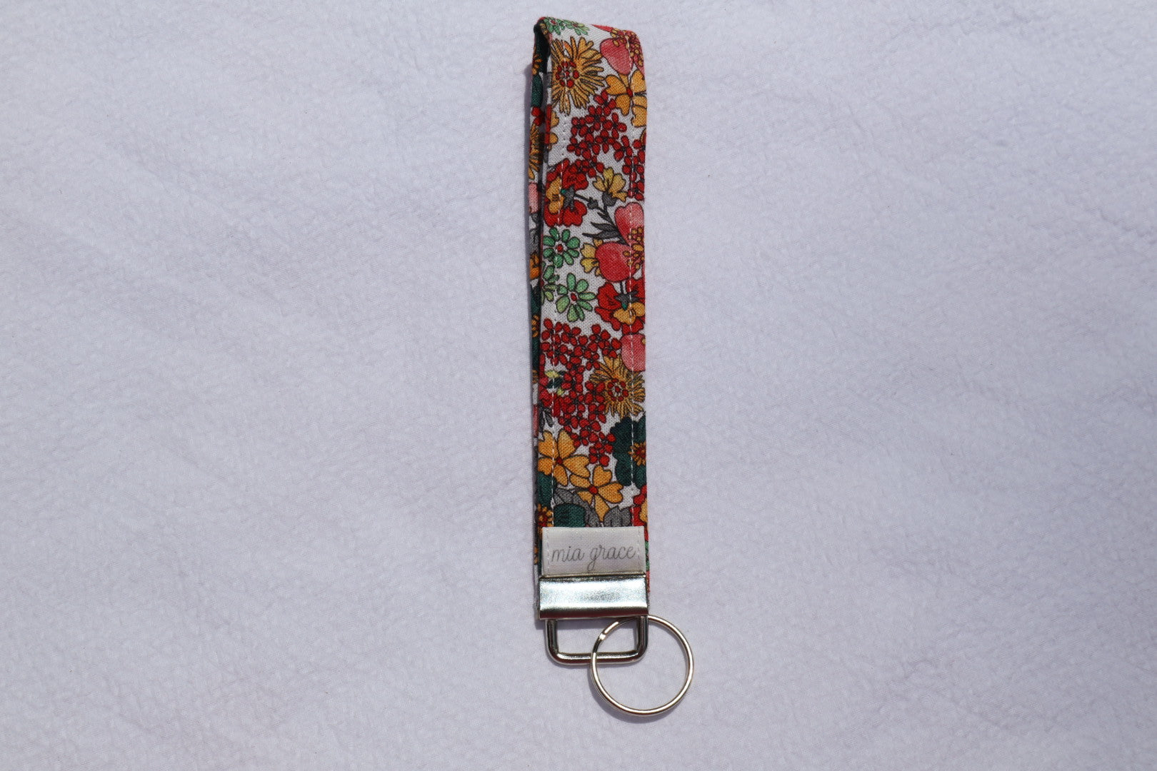 Fabric key fob with a yellow, blue, gray, and pink floral  patten with butterflies and a Mia grace brand label and a key ring
