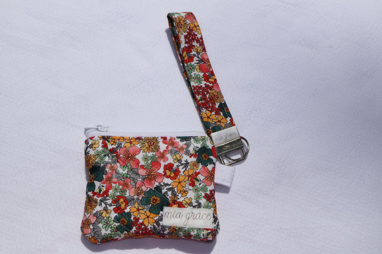 Fabric key fob with a yellow, blue, gray, and pink floral  patten with butterflies and a Mia grace brand label and a key ring with a matching wallet sold separately 