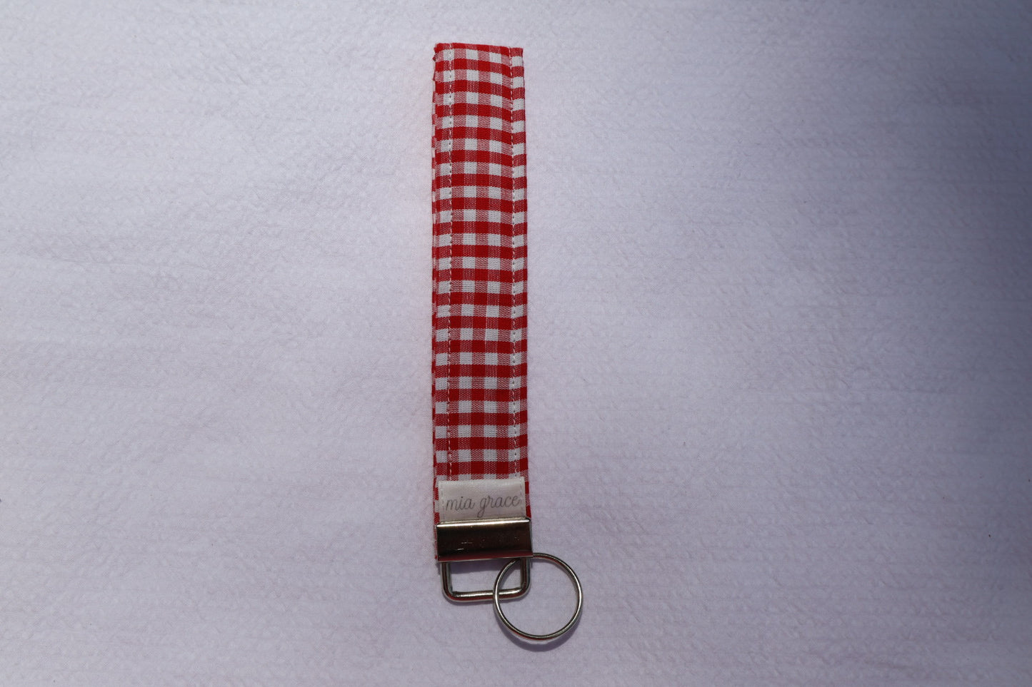 Fabric key fob with a red and white gingham  patten and a Mia grace brand label and a key ring
