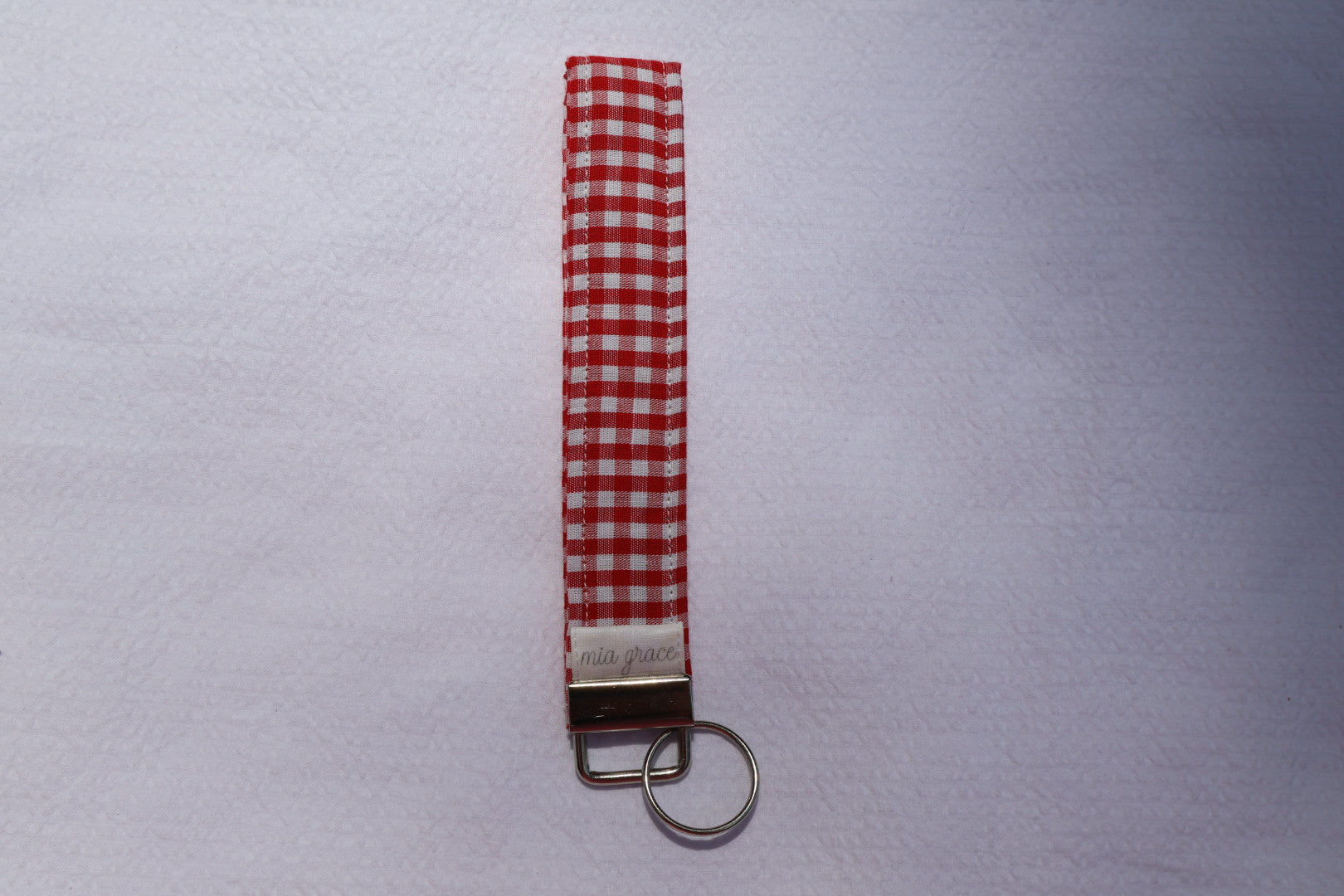 Fabric key fob with a red and white gingham  patten and a Mia grace brand label and a key ring
