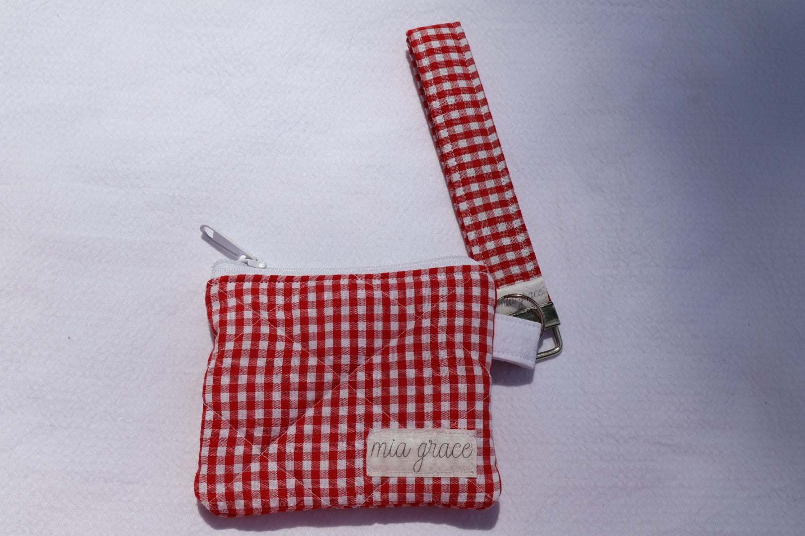 red and white gingham wallet sized pouch with a 'mia grace' brand label, zipper closure, and a hoop for a key ring to be attached. 