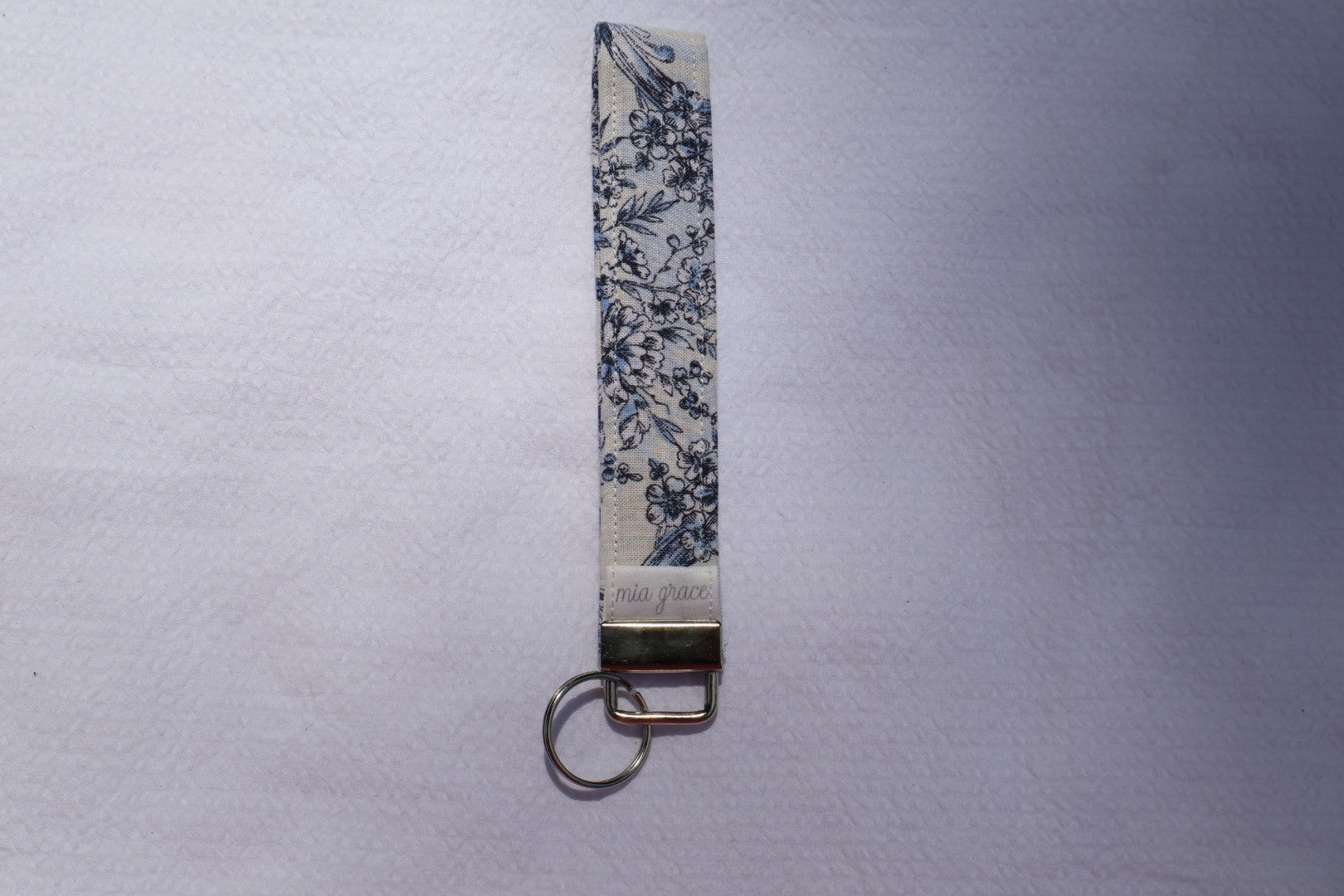 Fabric key fob with a blue floral patten and a Mia grace brand label and a key ring