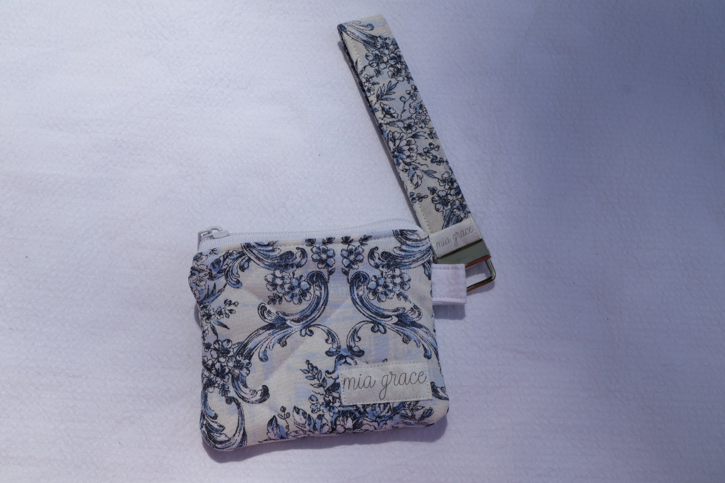 Fabric key fob with a blue floral patten and a Mia grace brand label and a key ring with a matching wallet that is sold separately.