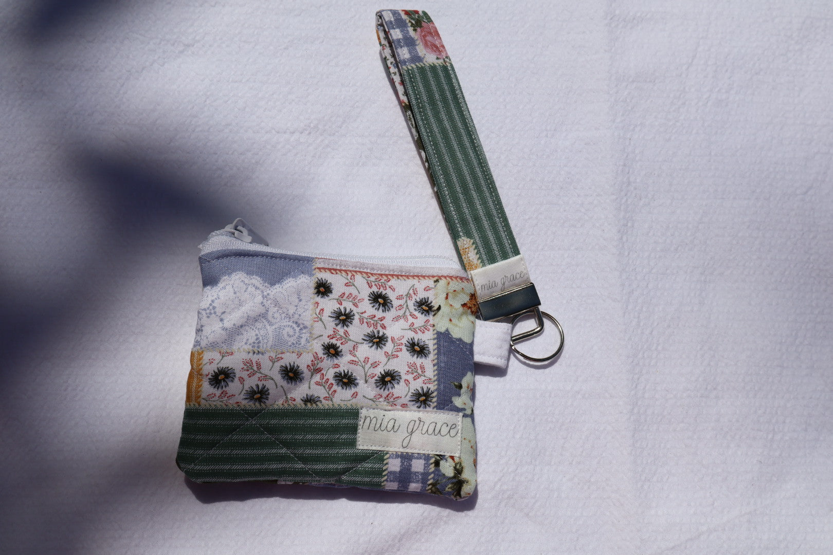 patchwork fabric wallet sized pouch with a 'mia grace' brand label, zipper closure, and a hoop for a key ring to be attached with a matching wristlet that is sold separately