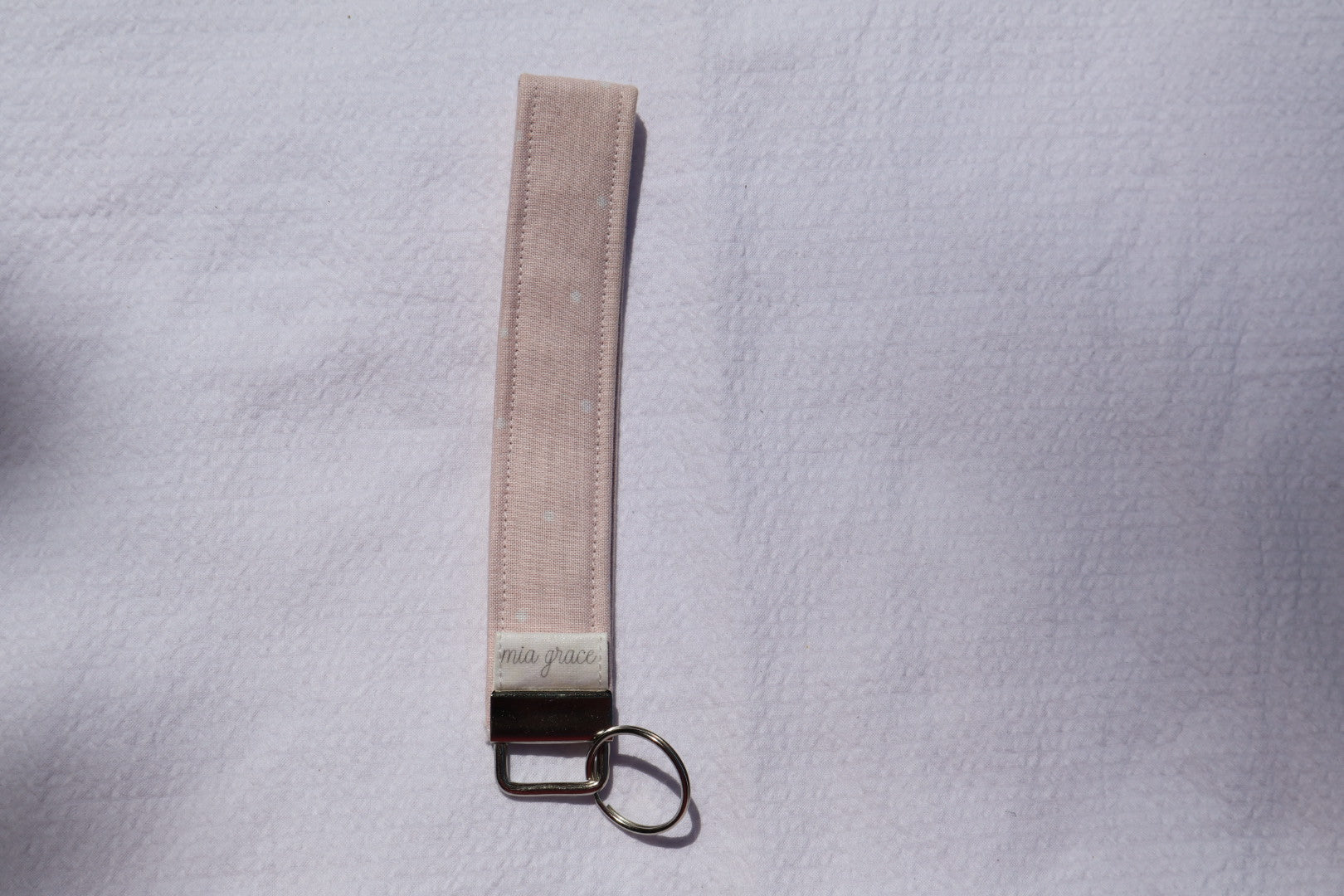 Fabric key fob with a pink fabric and white polka dots pattern and a Mia grace brand label and a key ring