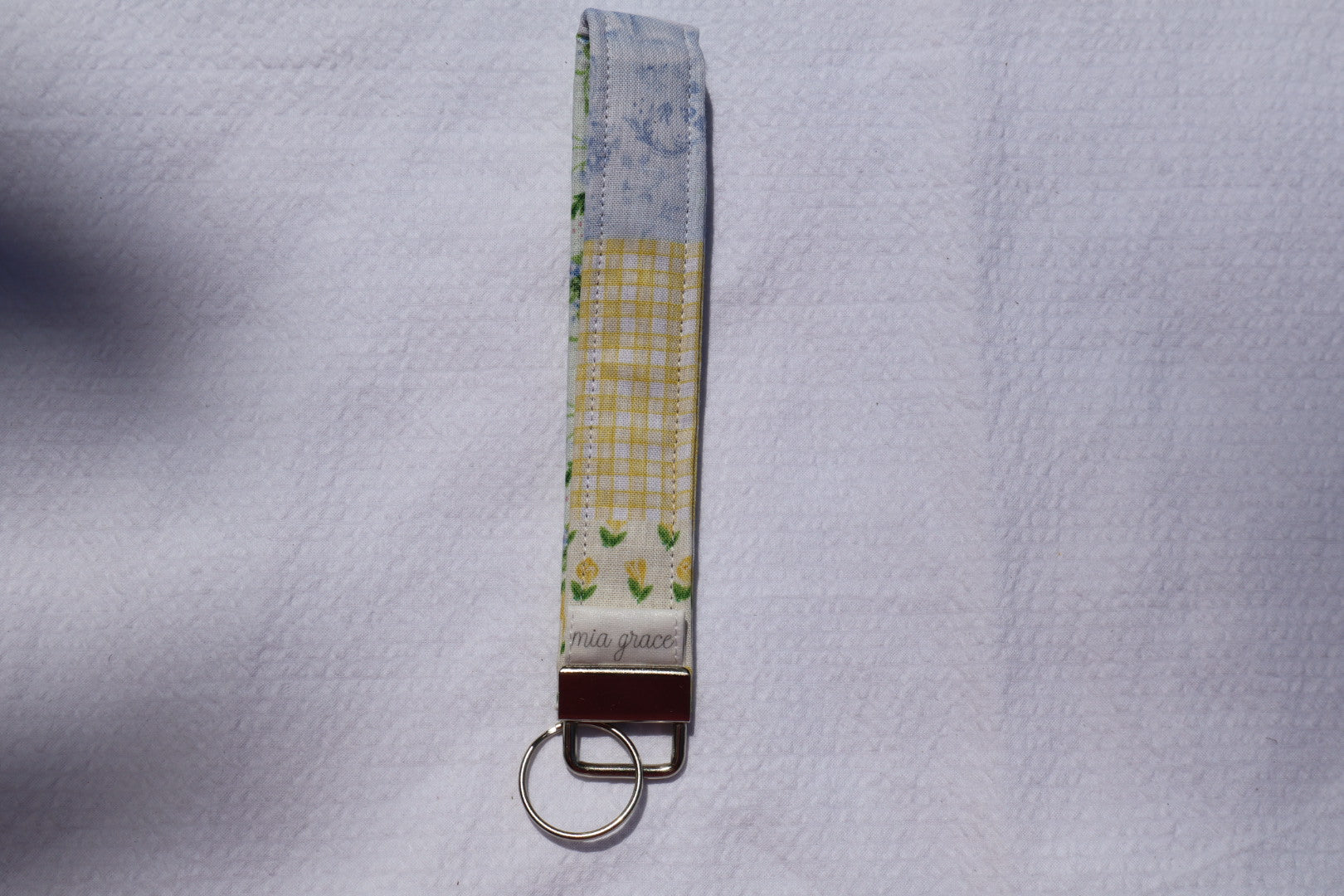 Fabric key fob with a patchwork yellow and blue floral pattern and a Mia grace brand label and a key ring